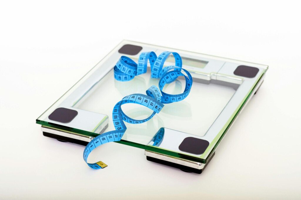 A bathroom scale with a blue measuring tape wrapped around it, all against a plain white background.