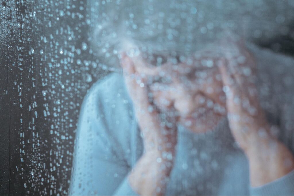 depressed woman, obscured partially by water droplets on window