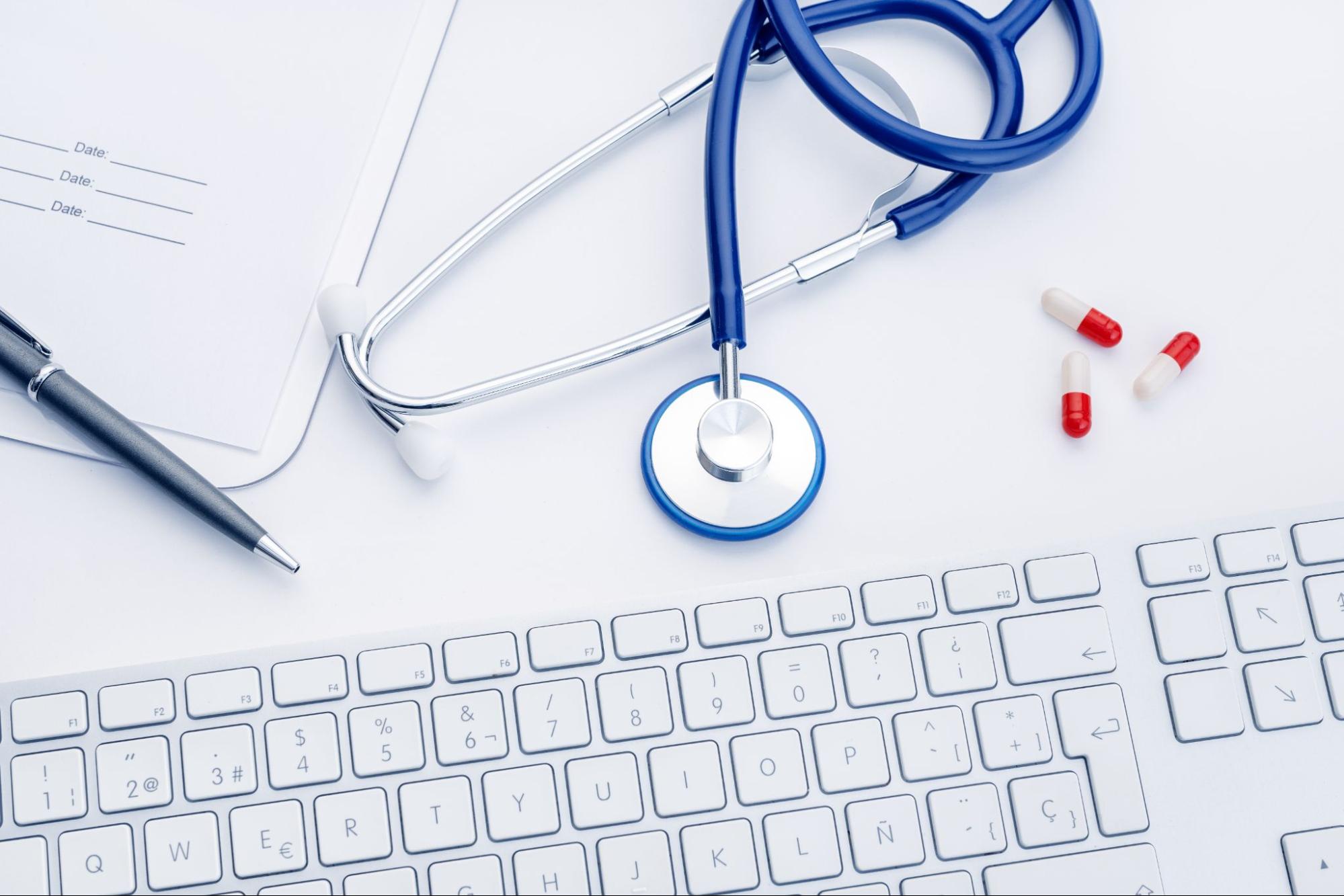primary care workspace with stethoscope, keyboard, and prescription pills