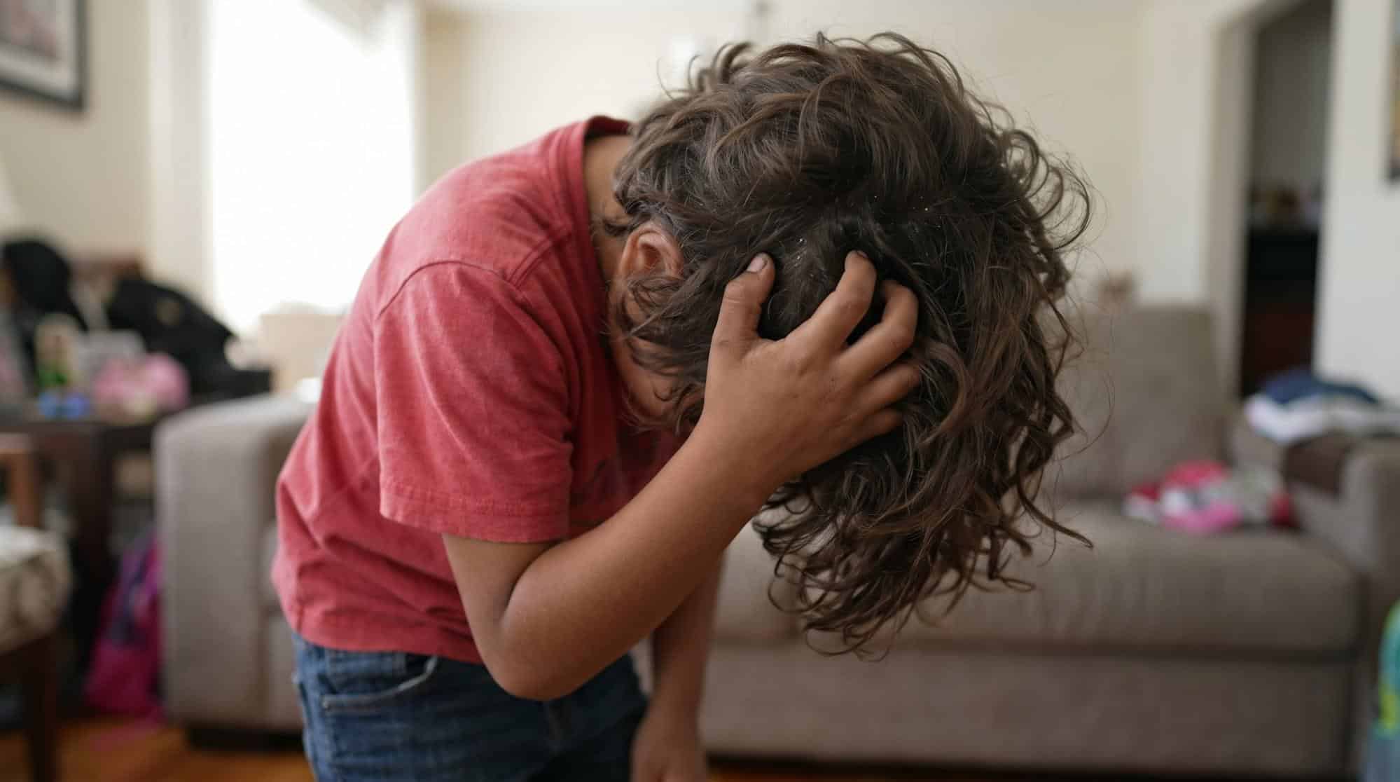 Child leaning forward and scratching his curly hair, illustrating a head lice issue requiring professional lice treatment in Weslaco, TX.