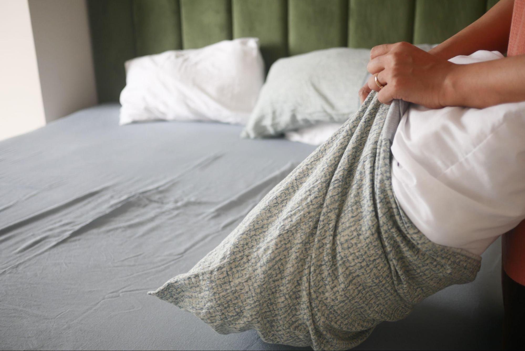 Person changing bedding as part of home cleaning to help prevent reinfection during scabies itch treatment.