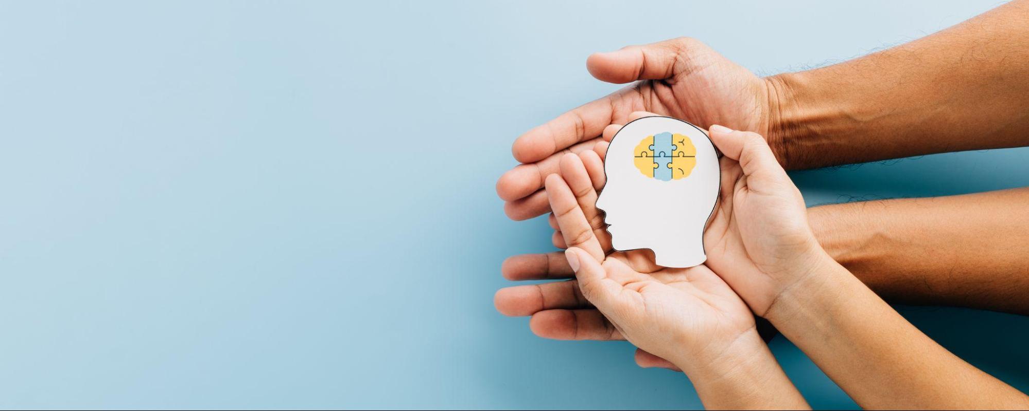 Hands holding a head-shaped mental health symbol with colorful puzzle pieces representing brain health and emotional well-being. 