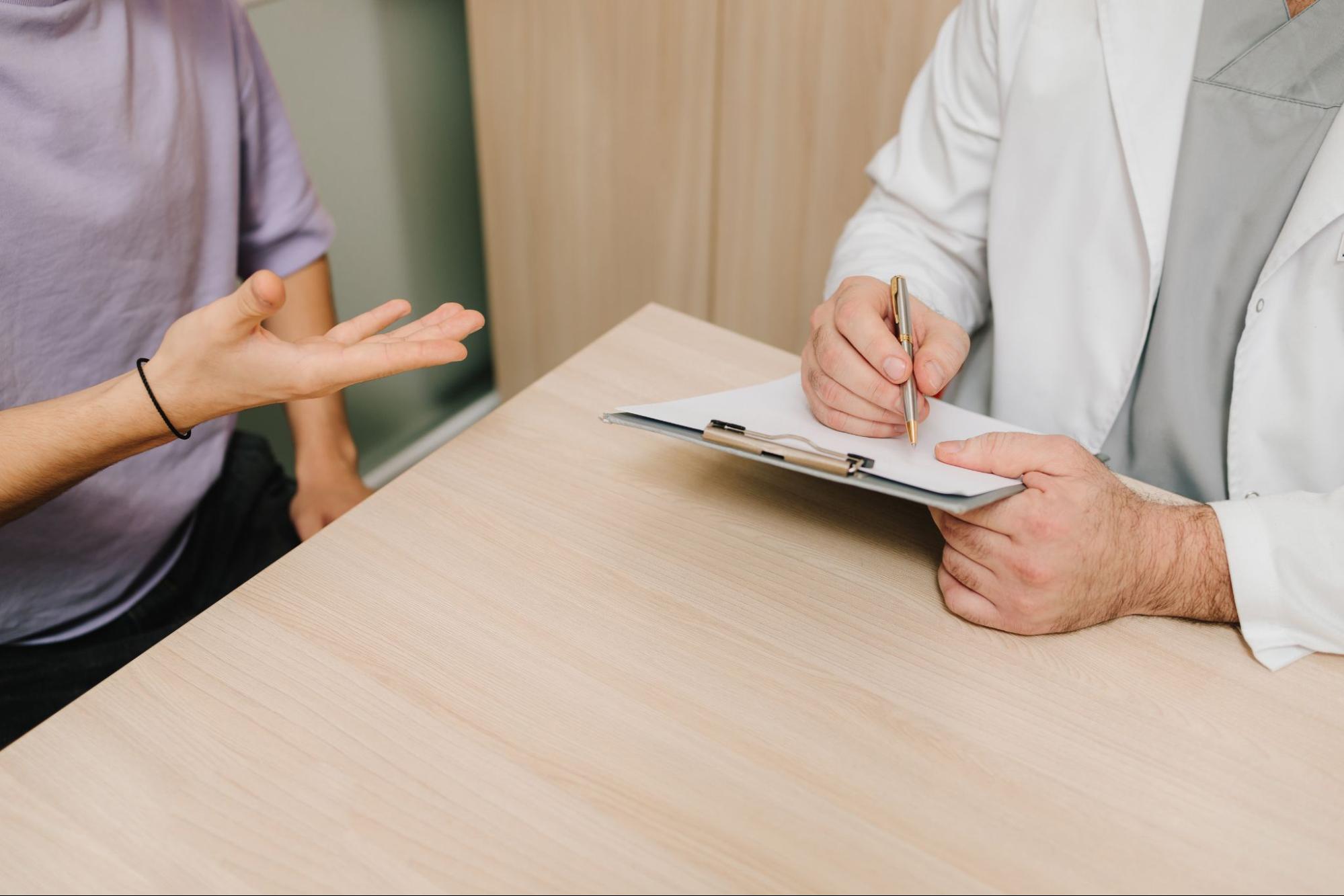 Physician taking notes while an adult patient discusses their medical history 