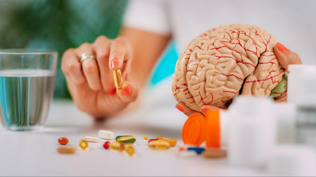Person holding a brain model beside medication, illustrating how ketamine affects the brain and its role in brain signaling. 