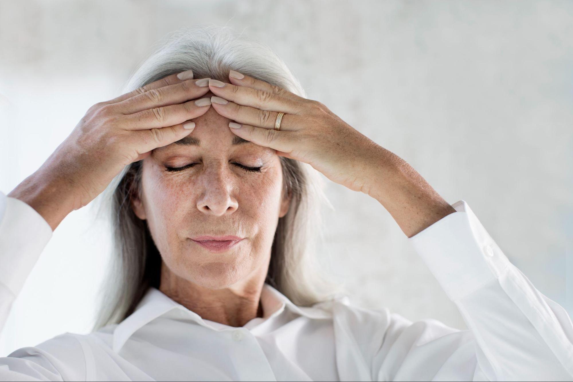 Older woman holding her temples while experiencing discomfort, illustrating symptoms considered when evaluating ketamine neuroplasticity treatment.